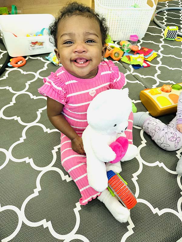 Child in pink striped outfit sitting on floor with a white stuffed animal