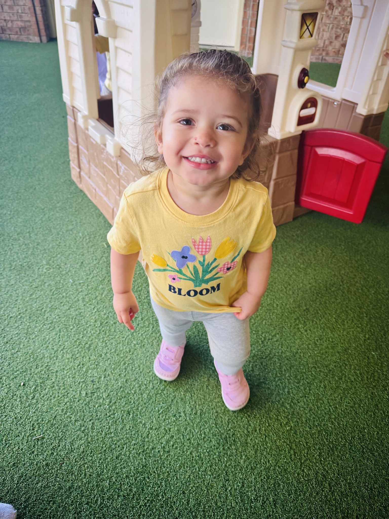 Child standing on green turf in front of a playhouse