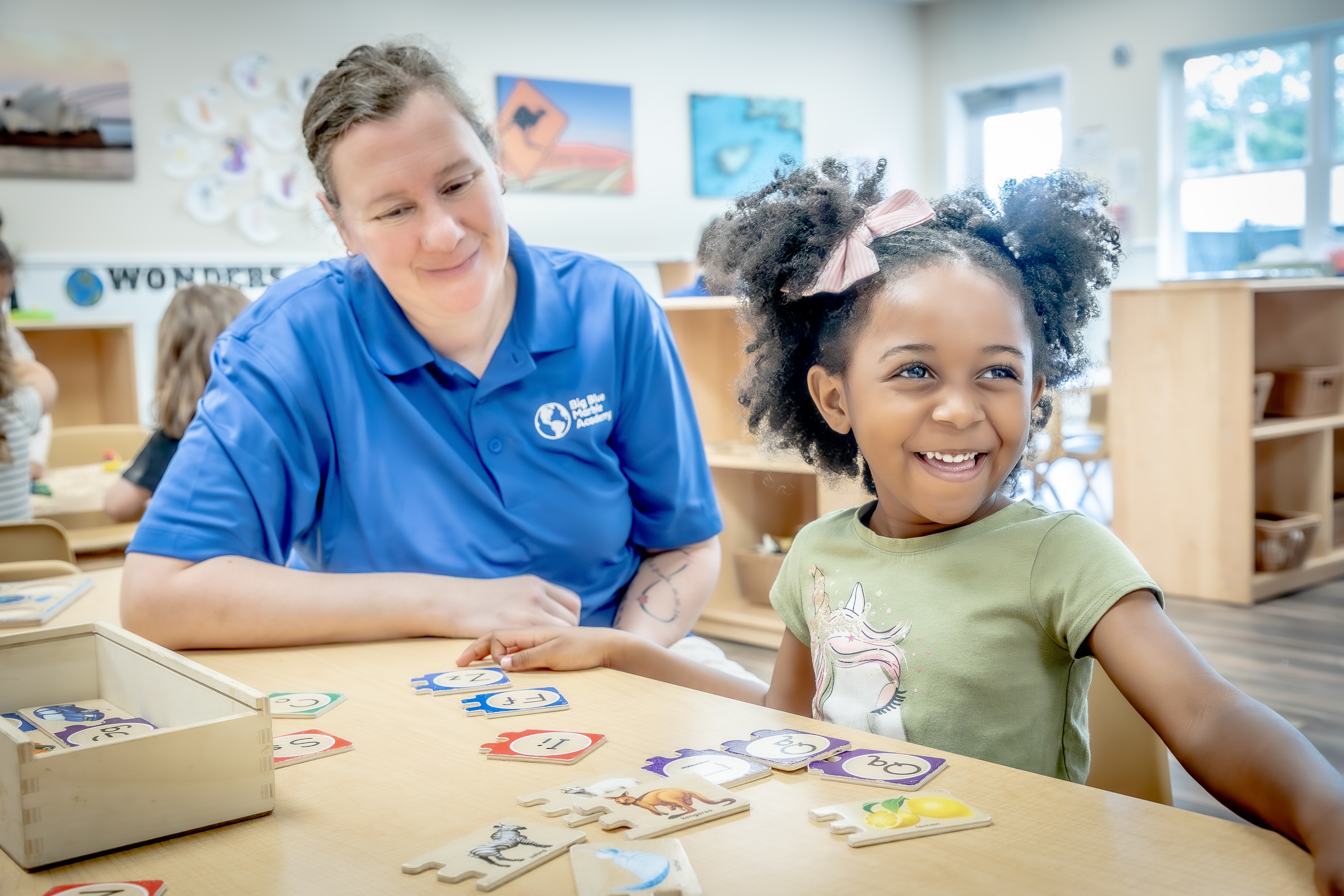 Adult and child playing with letter flashcards at a table in a classroom