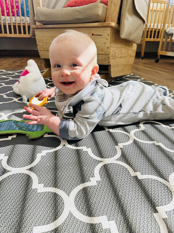Child on stomach on a patterned mat, holding a toy