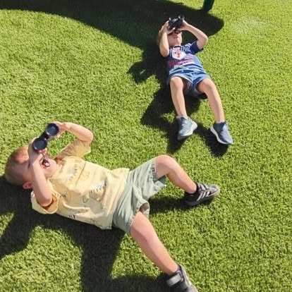 Two children lying on grass looking through binoculars