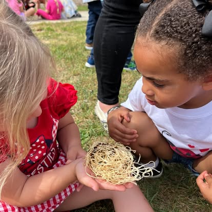 Two children looking at a small bird's nest held in a child's hand