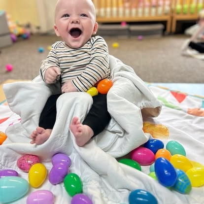 Child sitting on a blanket surrounded by colorful plastic eggs