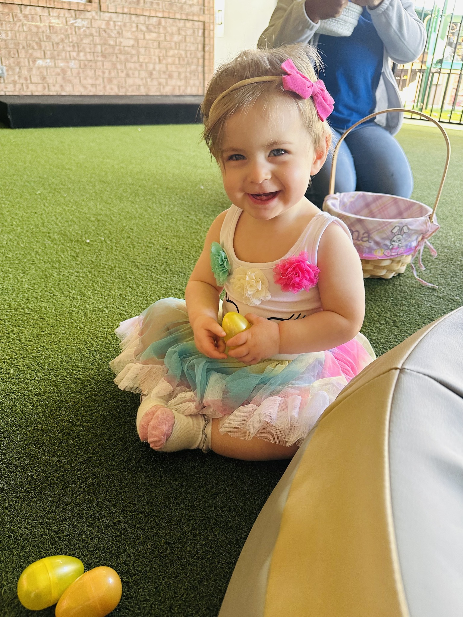 Child in a colorful dress sitting on grass holding a yellow egg