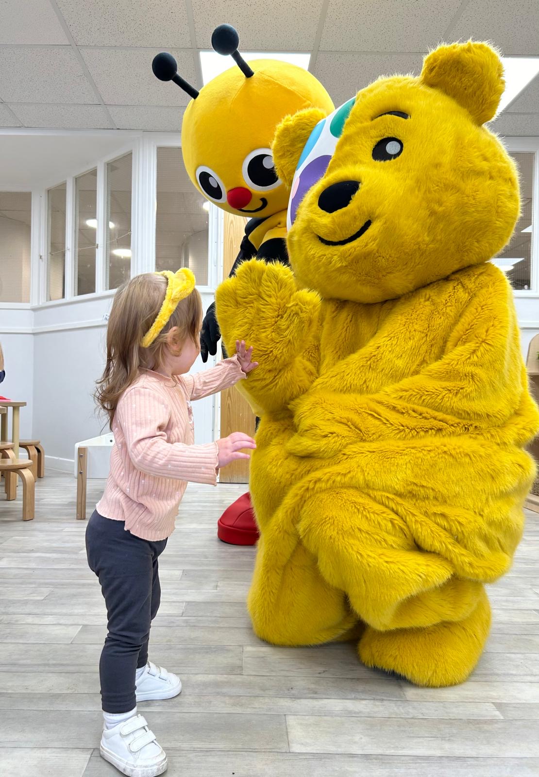 Child interacting with two mascots, one a yellow bear and the other a bee