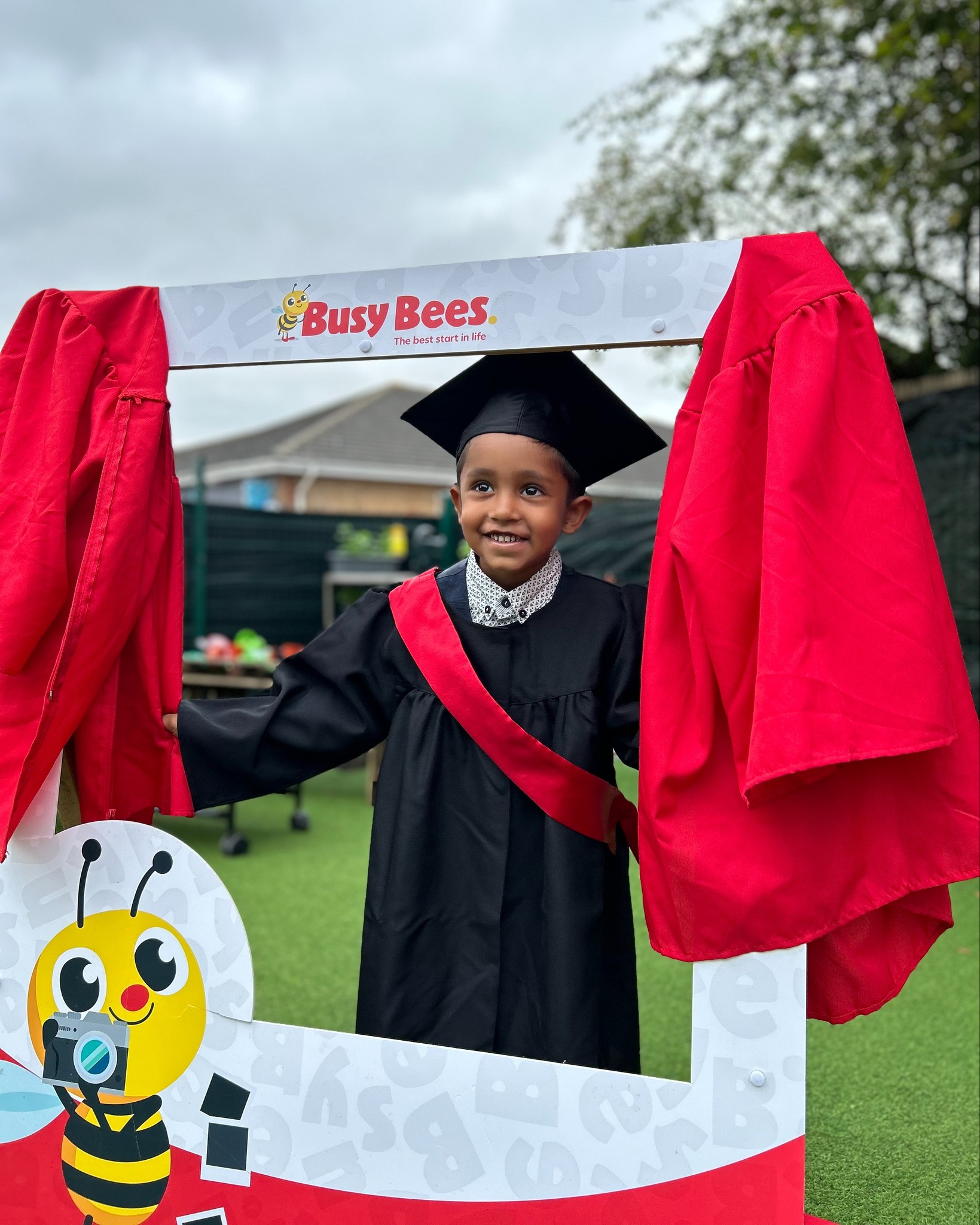 Child in graduation cap and gown standing in a photo booth frame