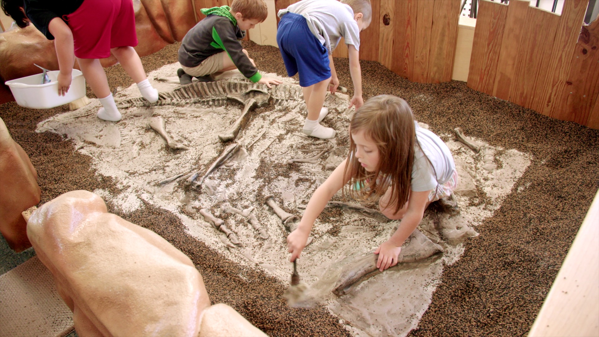 Children excavating faux dinosaur fossils in a sandbox