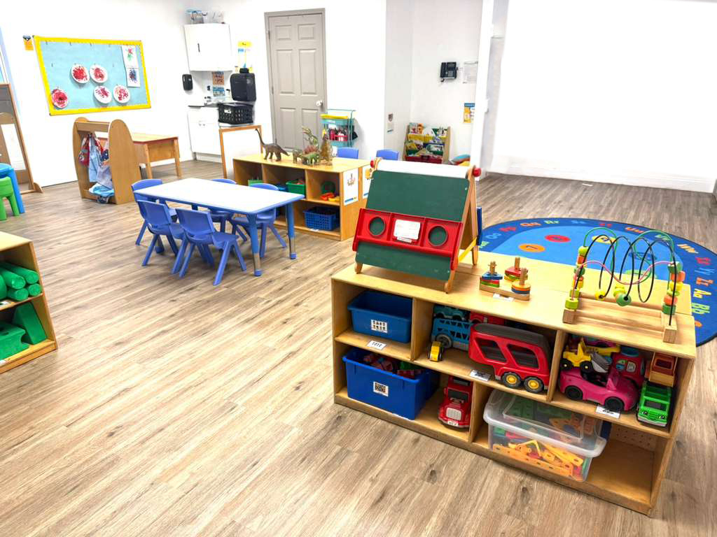 Classroom with toy shelves, children's tables and chairs, and play rugs