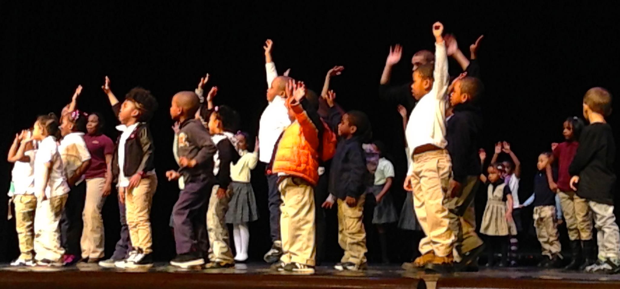 Group of children on a stage with some raising their hands