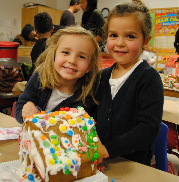 Two children with a decorated gingerbread house