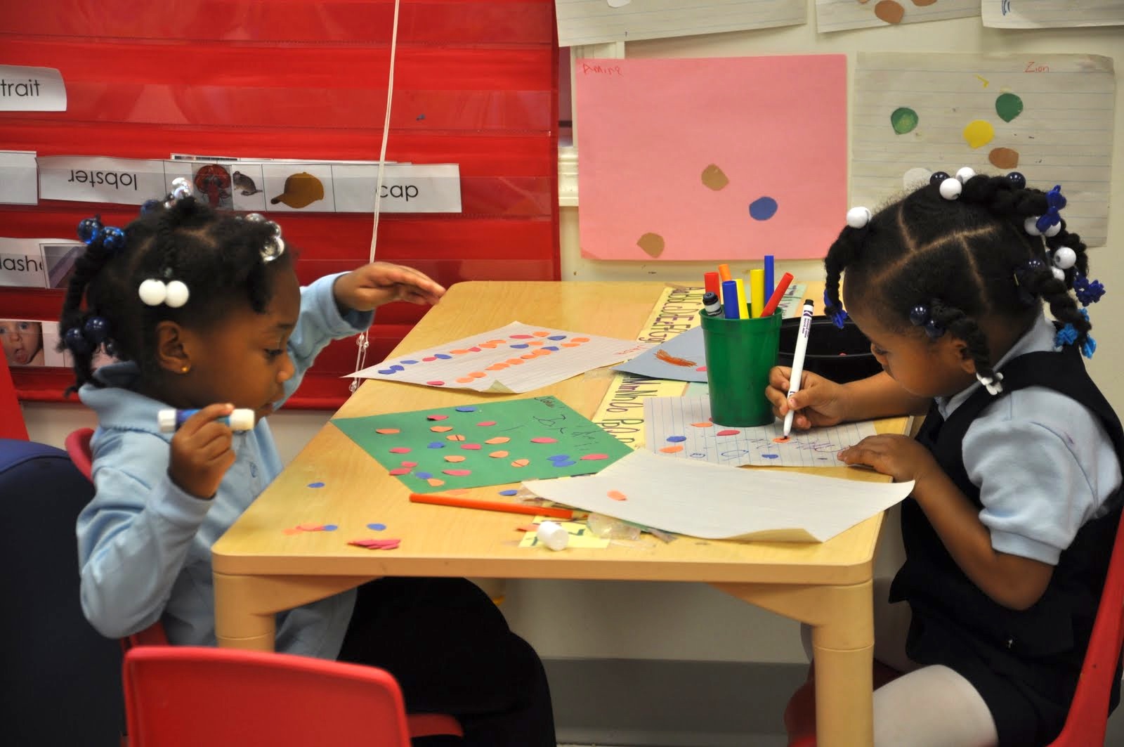 Two children drawing and coloring at a table in a classroom