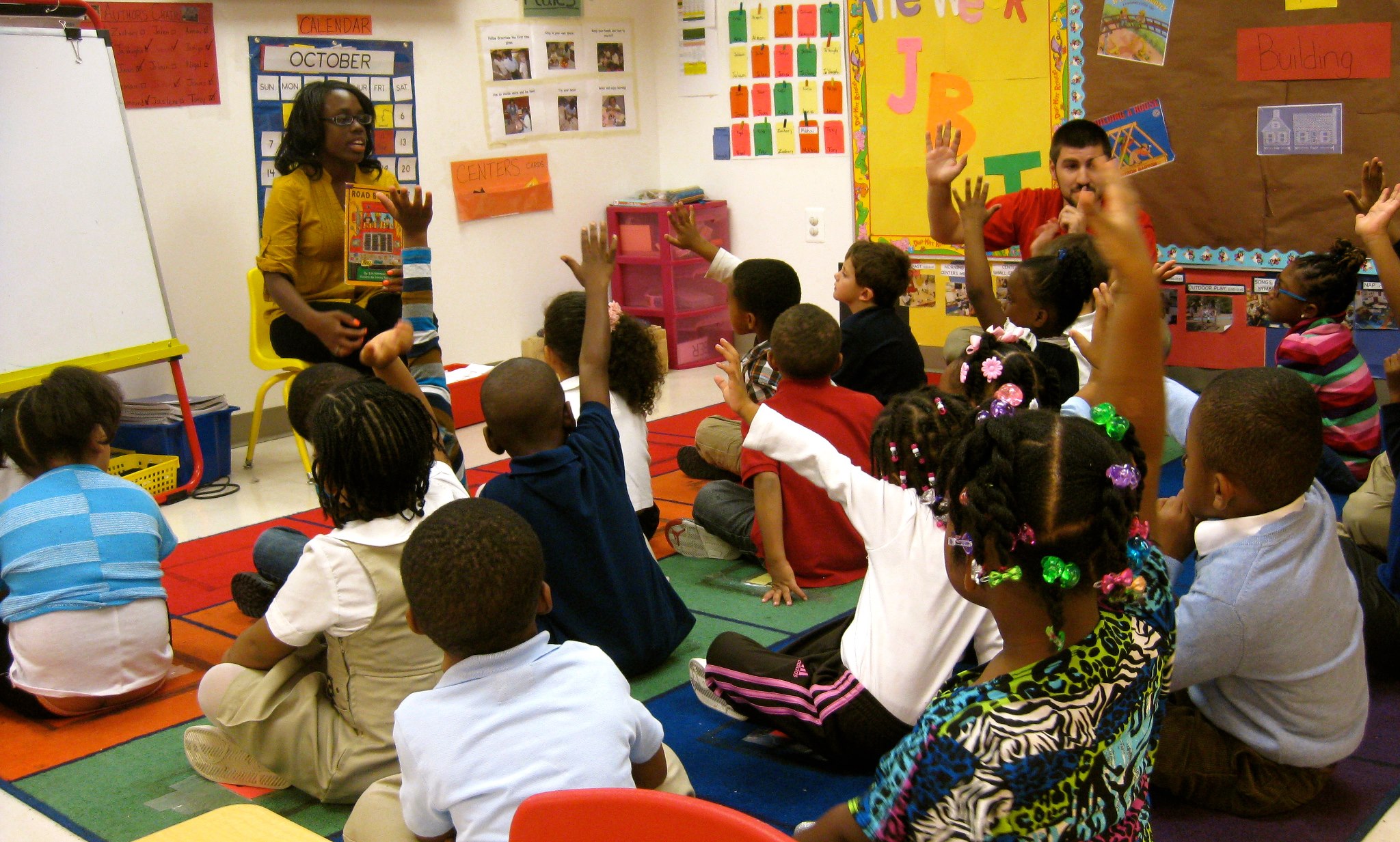 Adults and children in a classroom with hands raised