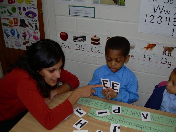 Person pointing to letters held by a child in a classroom