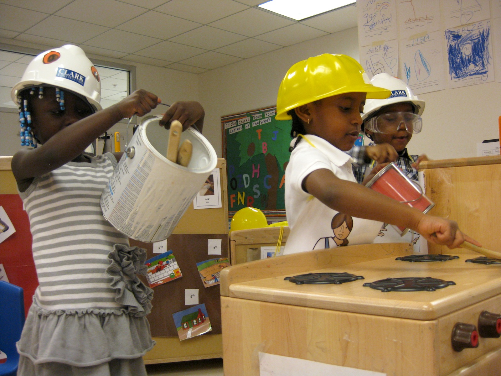 Children in hard hats playing with a toy stove and bucket