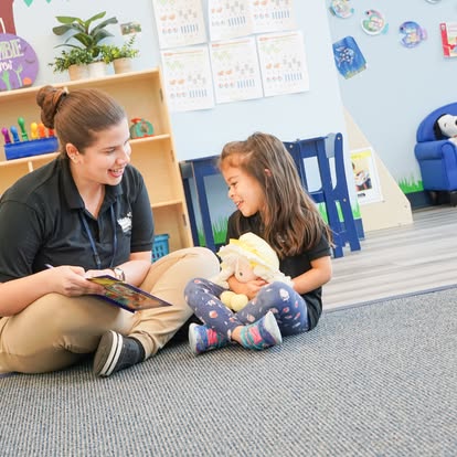 Adult and child sitting on a classroom floor looking at a book