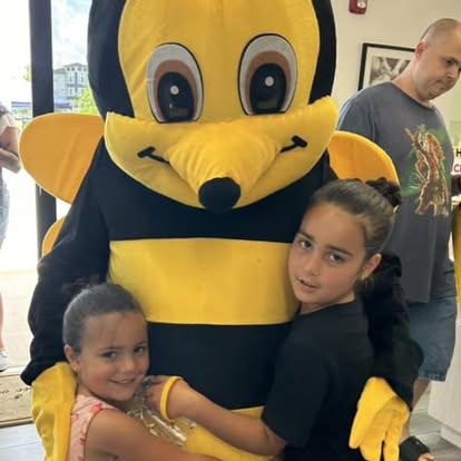 Two children hugging a large bee mascot