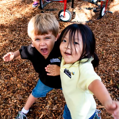 Two children standing on a wood chip playground