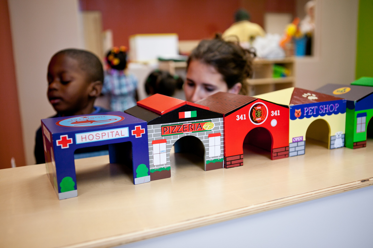 Child and person looking at toy buildings including a hospital and pizzeria
