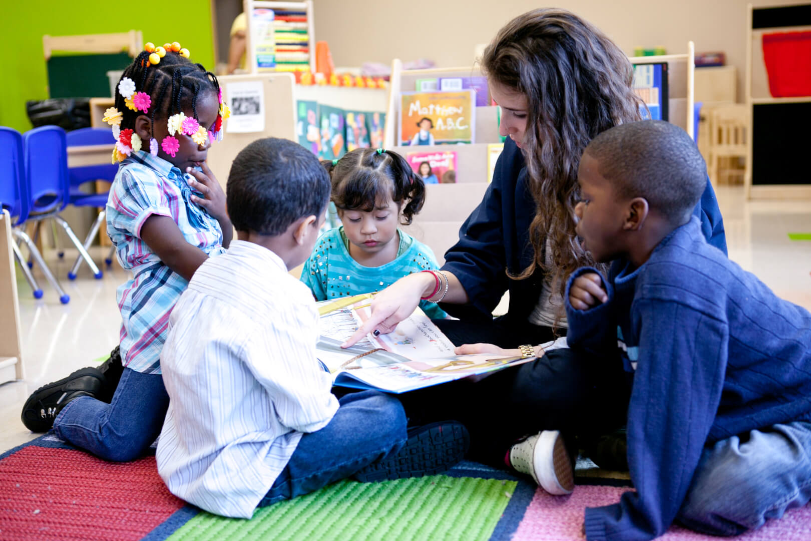 Adult reading a book to three children in a classroom