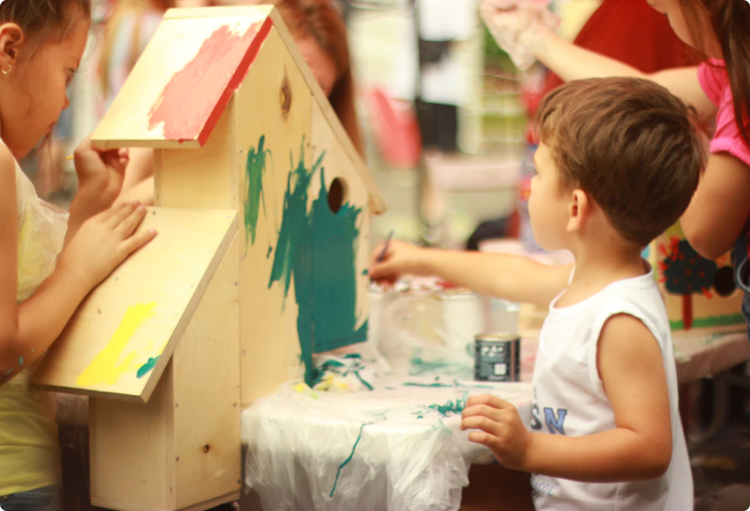 Two children painting a wooden birdhouse