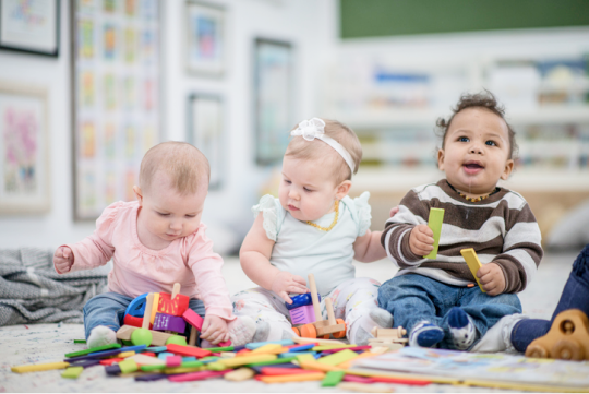 Three babies playing with colorful toys on the floor