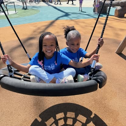 Two children sitting on a swing at a playground