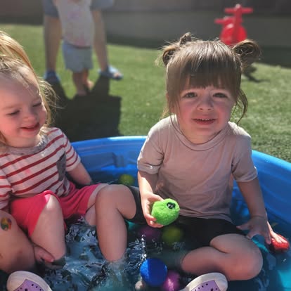 Two children sitting in a blue wading pool with water and toys