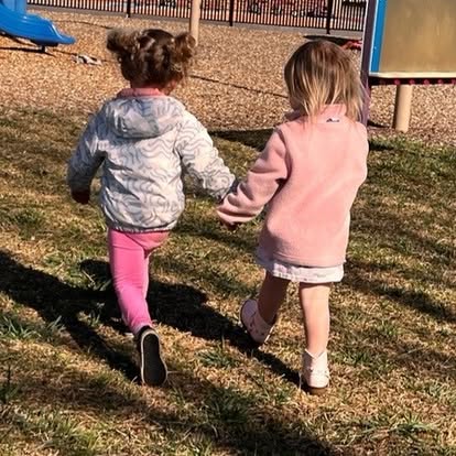 Two children holding hands and walking away from the camera in a park