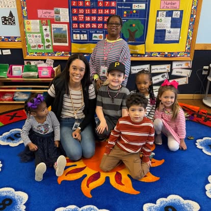 Two adults and five children posing in a classroom