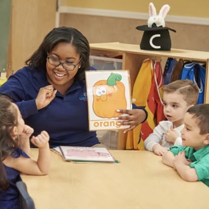 Person showing children a flashcard with an orange on it