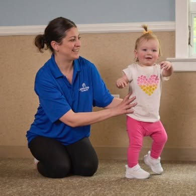 Person kneeling and supporting a child learning to walk