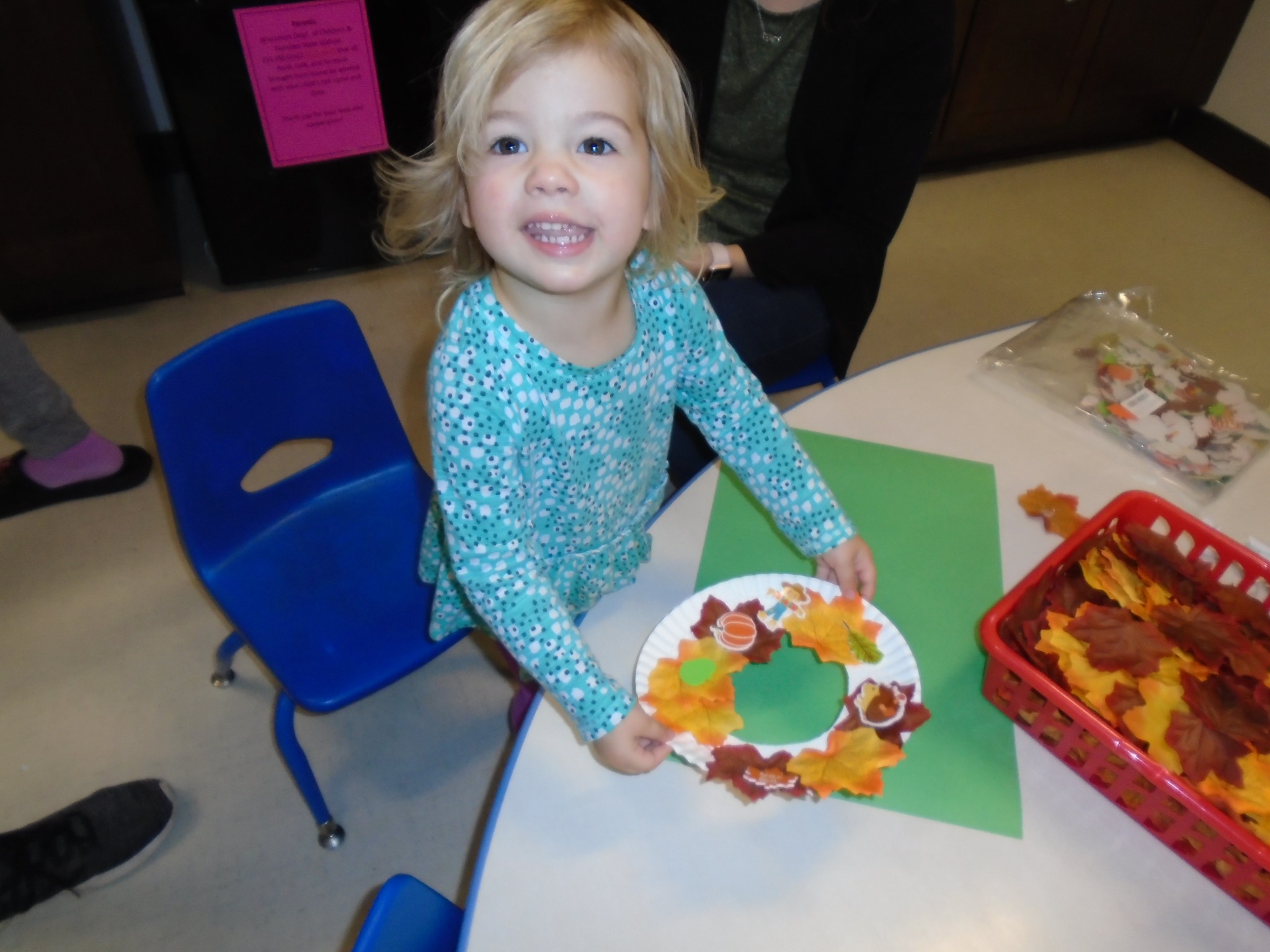 Child holding a paper plate craft with autumn leaves