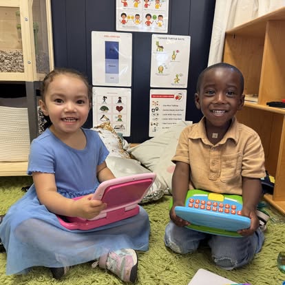 Two children sitting on the floor holding toy laptops