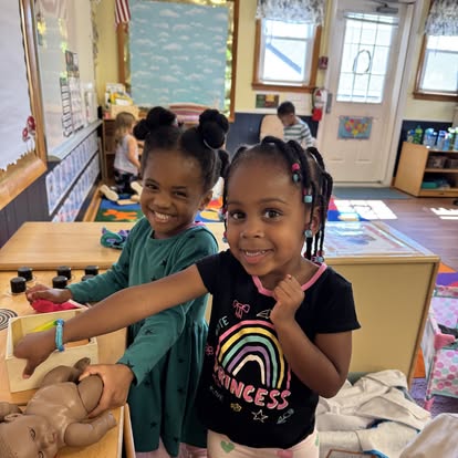 Two children playing with a doll in a classroom