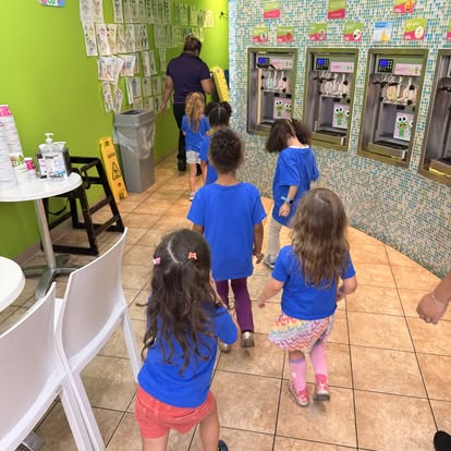 Children in blue shirts walking in a line past frozen yogurt machines