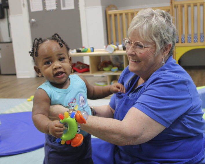 Adult person helping a young child stand and hold a toy