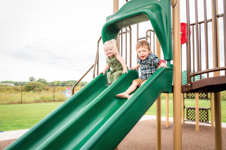 Two children on a green playground slide