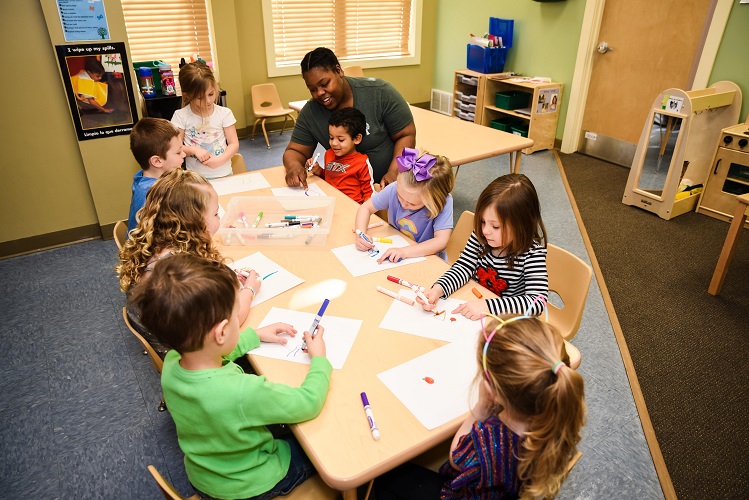 Adult and children drawing at a table in a classroom