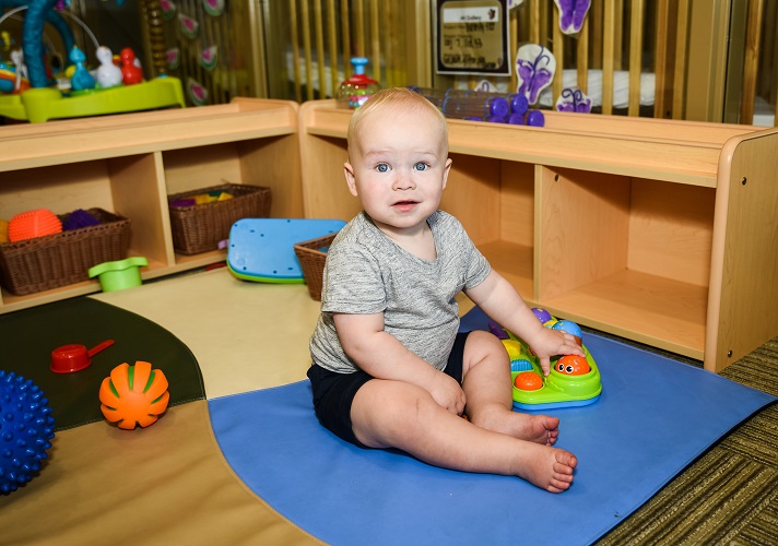 Child sitting on a blue mat playing with a toy in a classroom
