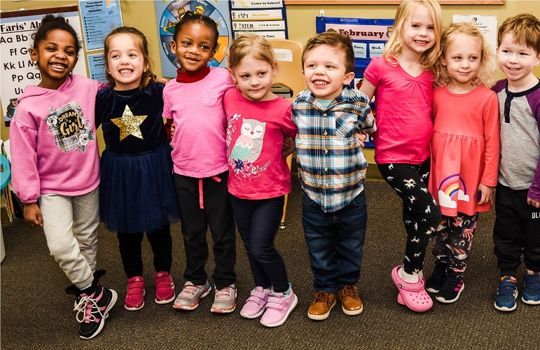 Seven children standing together in a classroom