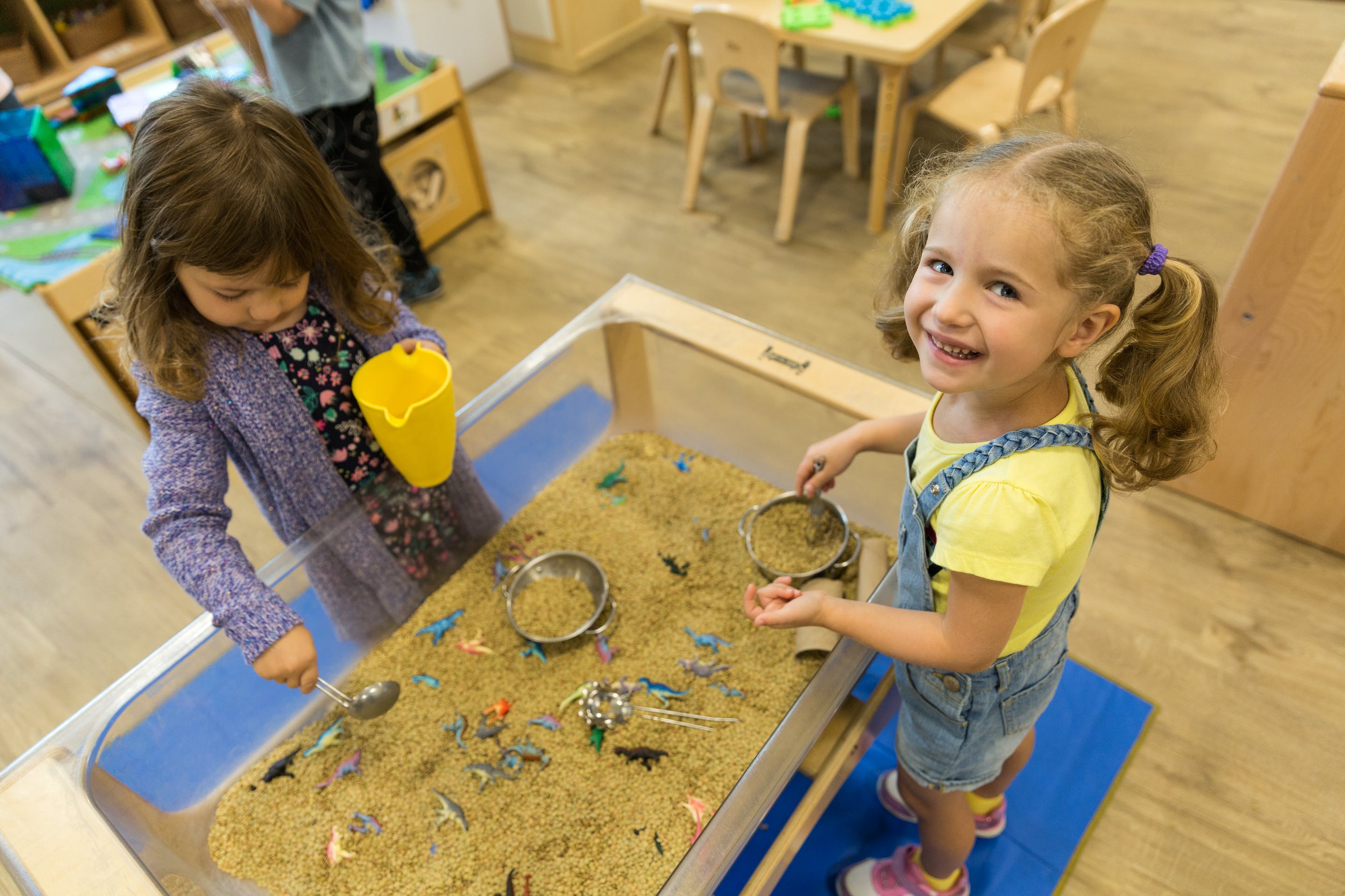 Two children playing with sand and toys in a sand table