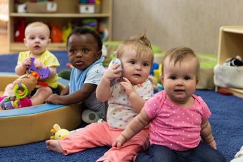 Four babies playing on a blue mat in a room