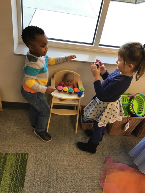 Two children playing with a baby in a high chair with toy cupcakes