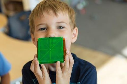 Child holding a green block in front of their mouth