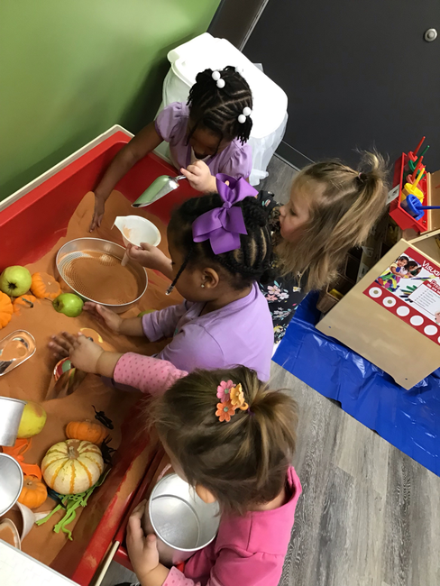 Children playing in a sand table with toy pumpkins and apples