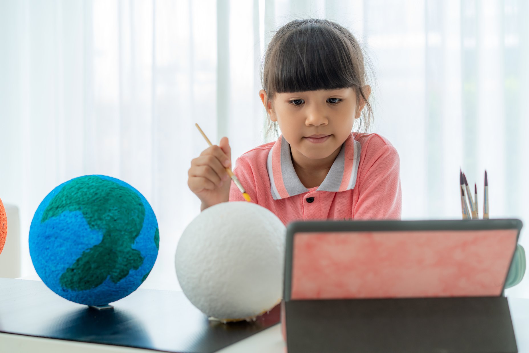 Child holding a stick, looking at a tablet with globes on a table