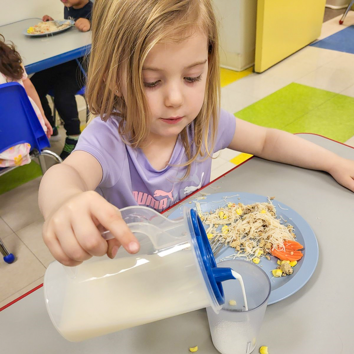 Child pouring liquid from a pitcher into a cup at a table
