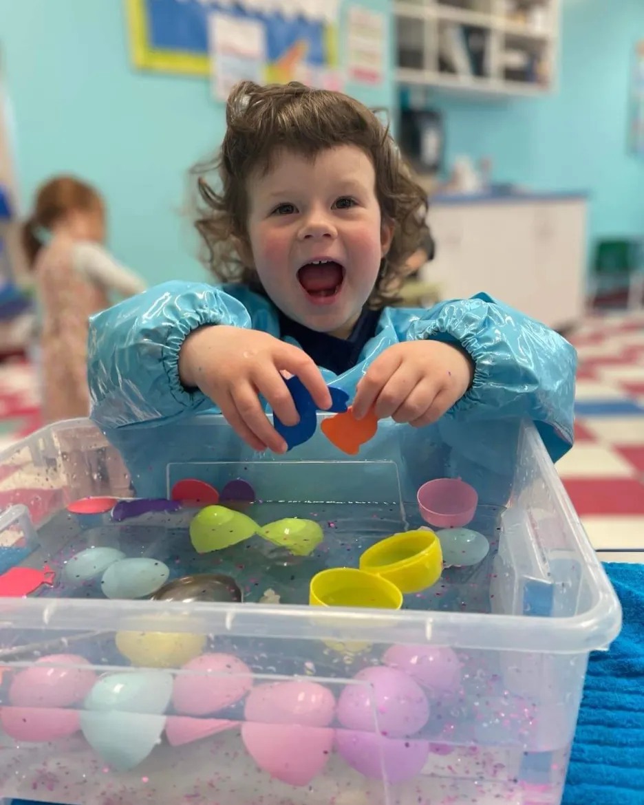 Child in smock playing with plastic eggs in a water bin