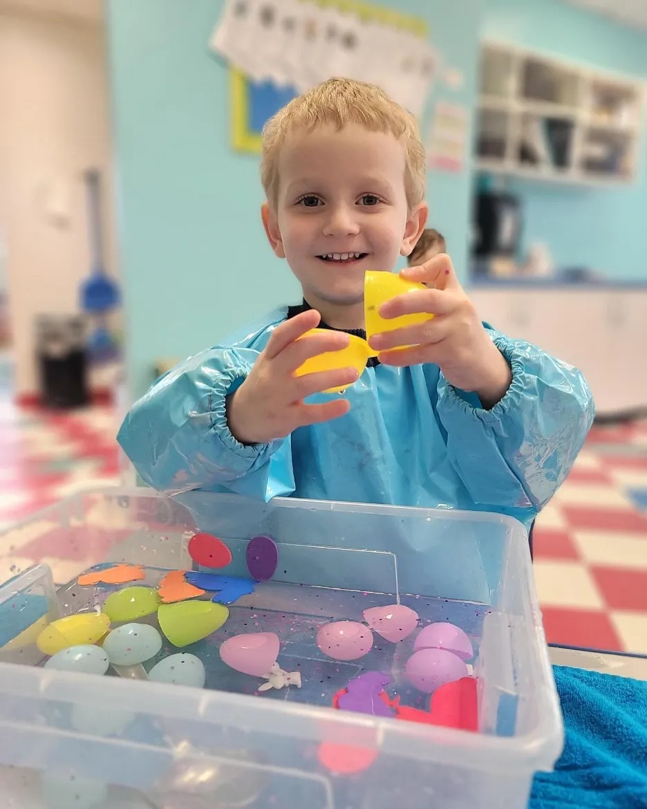 Child in smock holding yellow cups over a bin of water with colorful objects