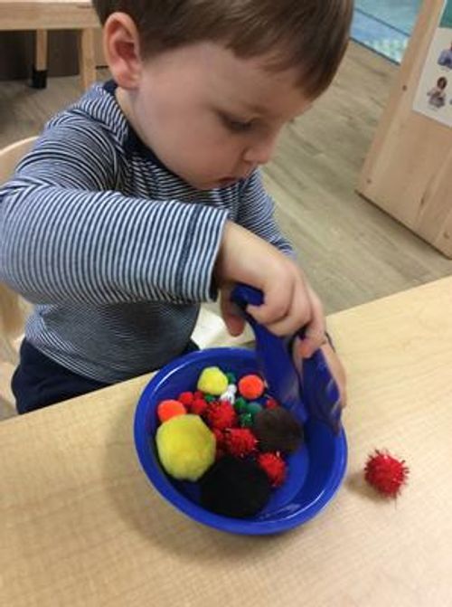 Child playing with colorful pom-poms in a blue bowl